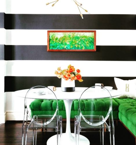 Ambiente com paredes listradas de preto e branco, sofá verde e cadeiras em acrílico transparente de Philippe Starck.