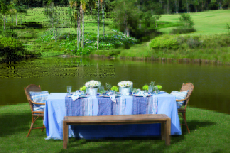 Inspirações para se criar mesas caprichadas. Mesa rustica com toalha azul de linho e banco, no meio do gramado na beira do lago.