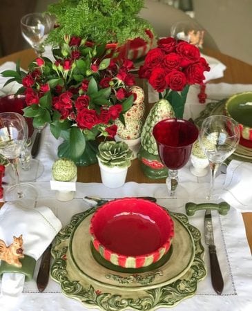 mesa decorada de Natal com pratos e potes em cerâmica vermelha e verde e arranjos com rosas vermelhas.
