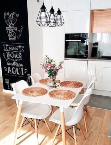 Cozinha aberta, mesa branca com cadeiras brancas e ao lado uma parede de lousa com desenhos em giz de cactos 