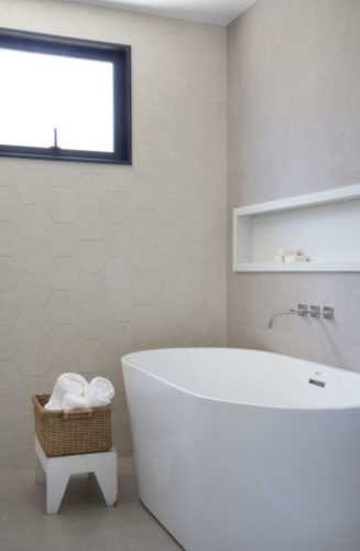 Banheiro claro, com uma banheira branca de piso perto da parede.