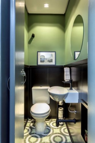 lavabo com meia parede revestida em madeira e pra cima pintado de verde abacate, no piso, ladrilho hidráulico. 
