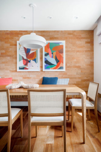 Sala de jantar com a parede de fundo revestida com tijolinhos da cor terracota.