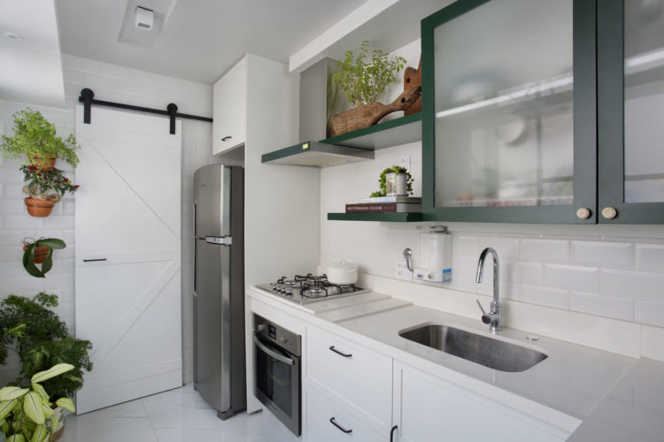 Cozinha com posta de correr em madeira , tudo branco menos o armário superior na cor verde.