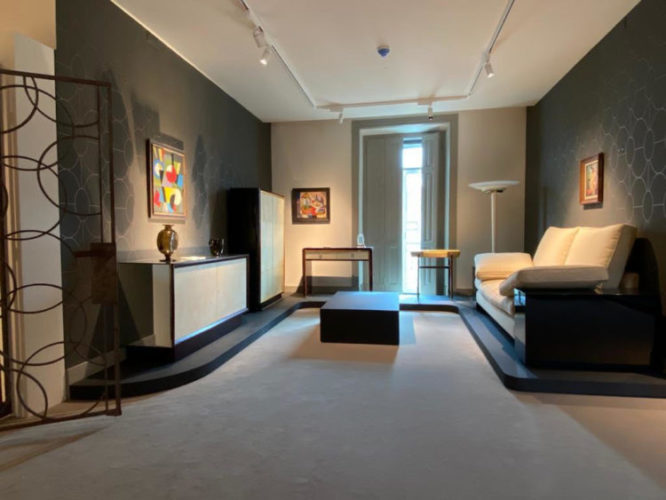 Sala no museu, B MAD, Berardo - Museu Art Déco em Lisboa. Papel de parede cinza com arabescos, sofá e um portão de ferro.