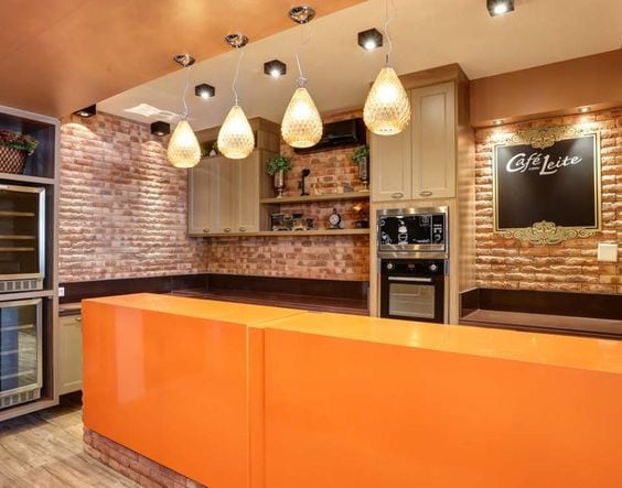 Cozinha com parede em tijolinhos e ilha laranja.