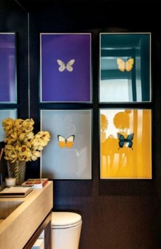 Lavabo decorado com quadros de borboletas com fundo colorido. Contraste bonito na parede preta.
