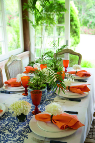 Inspirações para se criar mesas caprichadas. Mesa longa com caminho de mesa central azul e guardanapos laranja.