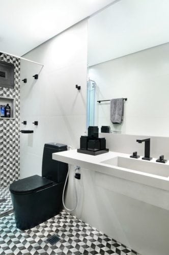Banheiro decorado revestimento do box e piso em preto e branco, bancada em Corian branco e louças e metais em preto.