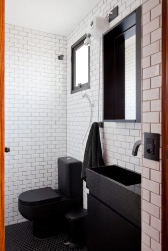 Banheiro com revestimento branco e louças e metais pretos.