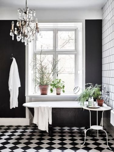 Banheiro decorado em preto e branco. Piso xadrex e paredes pintadas de preto fosco.