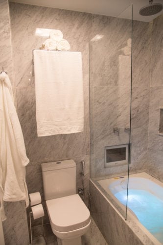 Baixo custo e hightech, proposta do apartamento decorado de 58m2. Banheiro revestido em mármore, com banheira de cromoterapia e tv na parede.
