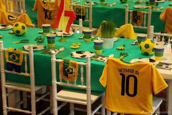 Dicas e inspirações para receber em casa nos jogos da Copa do Mundo 2022. Mesa com toalha verde, uma camisa do time do brasil com o nome neymar vestindo uma cadeira