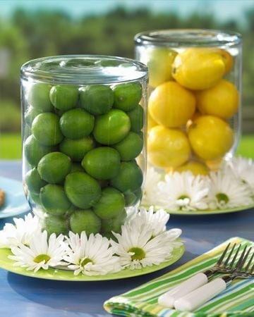 Arranjo para mesa. Limão galego e limão siciliano dentro de uma pote de cabeça para baixo e flores, tipo margarida enfeitando 