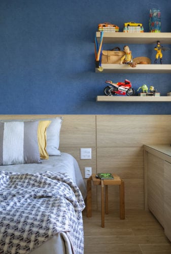 Quarto de criança, com parede pintada de azul e cabeceira em madeira ao longo da parede.