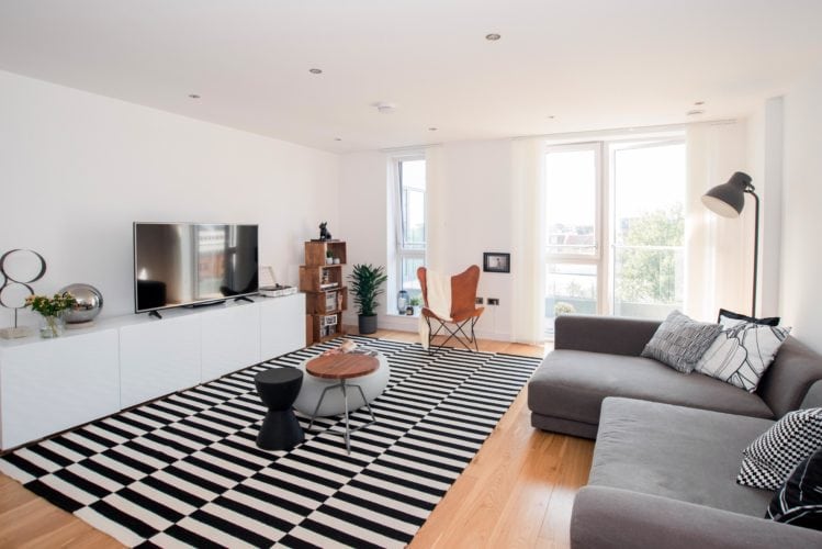 Arquitetas cariocas assinam o décor de apartamento em Londres. Sala ampla, com tapete preto e branco e sofá cinza.