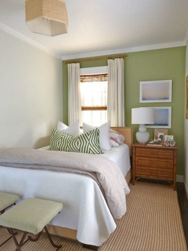 Cama embaixo da janela em um quarto pequeno , com parede verde e criado mudo ao lado da cama.