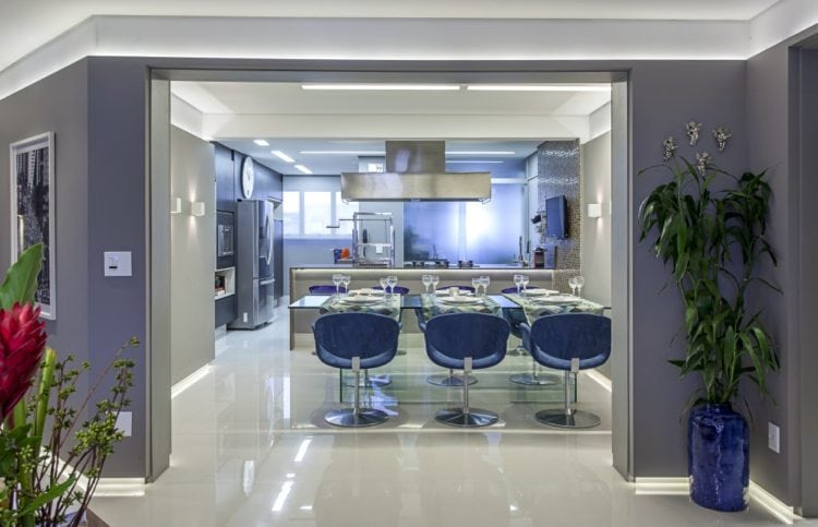 Cozinha aberta para a sala, com mesa de vidro e cadeiras na cor azul.