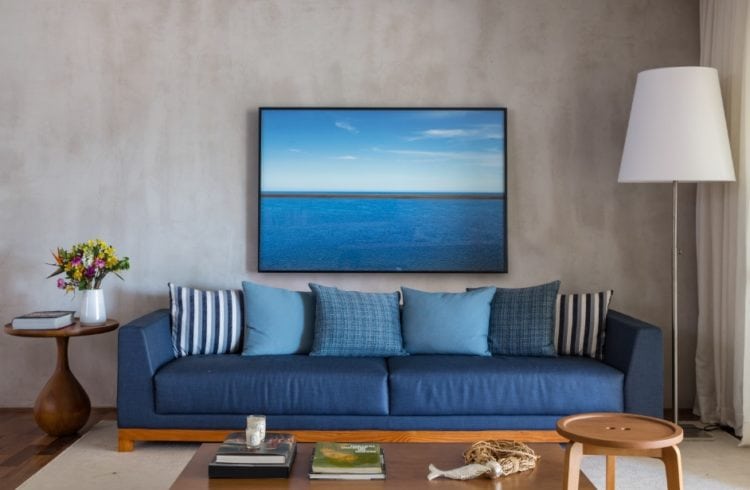 Sala com parede em cor de concreto e sofá azul com luminária de pé ao lado
