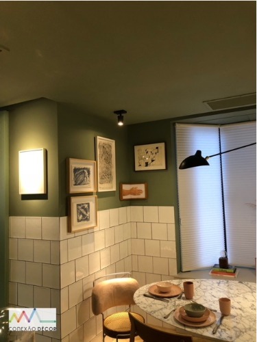Cozinha com meia parede em azulejo branco, parede pintada de verde e quadros na parede.