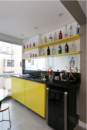 Varanda integrada a sala. Bancada com cooktop e armários amarelos.