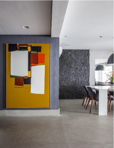 Urbanidade dá o tom para apartamento de família em SP. Parede cinza recebeu uma tela com fundo da cor mostarda com pintura moderna.