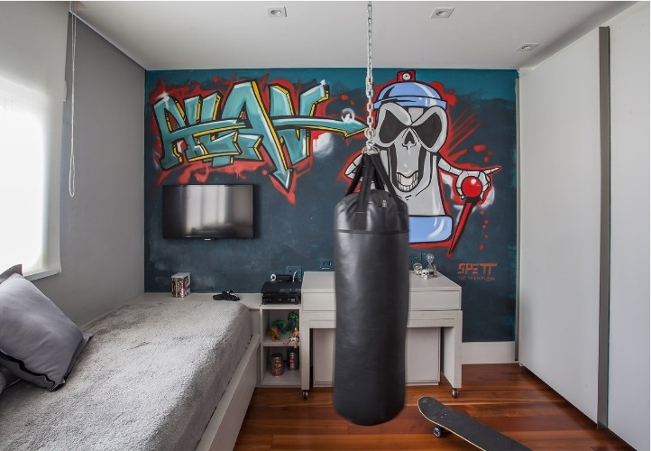 Urbanidade dá o tom para apartamento de família em SP. Quarto do filho decorado em tons de cinza, um grafitti na parede de fundo e um saco de boxe pendurado no meio do quarto,