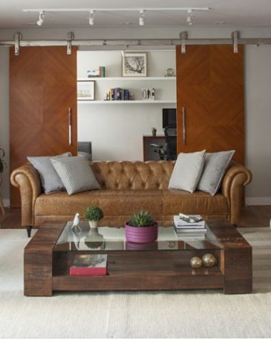 sala com sofá de couro e portas de correr ao fundo no projeto assinado por Bruno Moraes