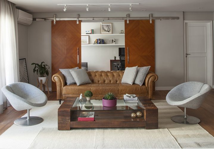 sala com sofá de couro e portas de correr ao fundo no projeto assinado por Bruno Moraes