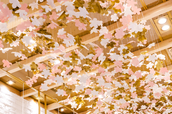 Penduradas no teto em módulos aramados, cerca de 2.500 pequenas flores confeccionadas pela artesã Rita Aranha foram pintadas individualmente nas cores dourado, rosa nude e branco, garantindo a personalidade e a identidade visual da marca.