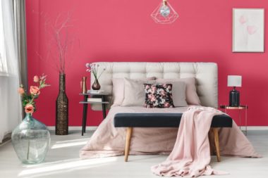 Pink flowers in glass vase near king-size bed with pink coverlet and violet pillows