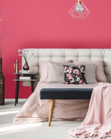 Pink flowers in glass vase near king-size bed with pink coverlet and violet pillows