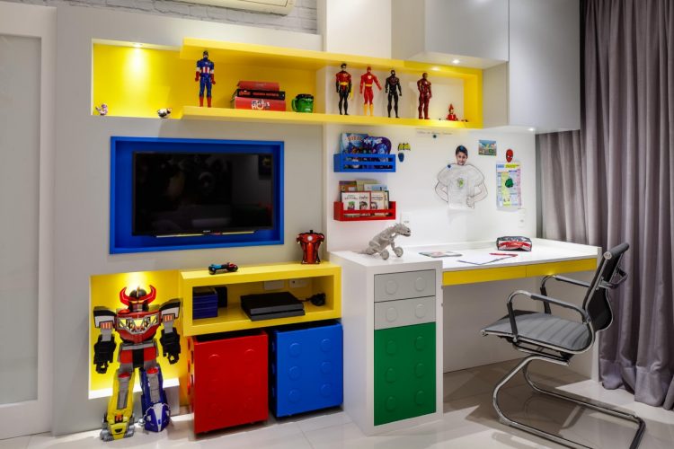 Estante de quarto de menino com nichos amarelo, azul e vermelho tendo o Lego como tema.