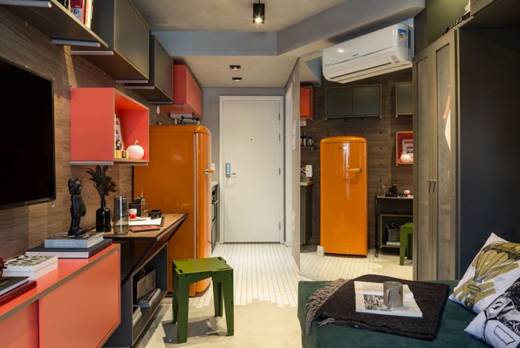 Cores vivas no décor com pegada industrial. Apartamento compacto com geladeira laranja e piso em cimento.