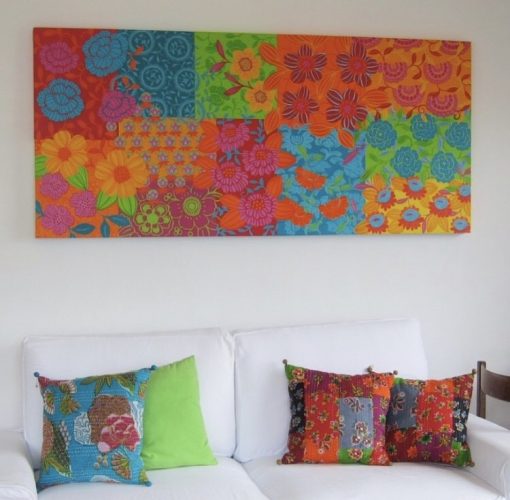 Mistura de estampas na decoração, sofá branco com almofadas coloridas e um quadro repleto de cor na parede em cima do sofá.
