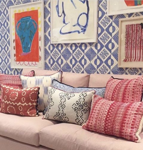 Mistura de estampas na decoração, parede com tecido azul e branco estampado, sofá rosa claro e almofadas nessas duas cores.