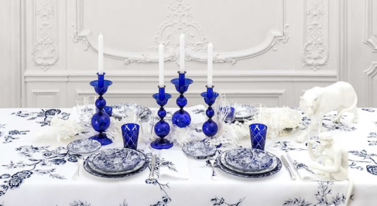 mesa posta com toalha branca bordada com flores azuis, copos e castiçais de vidro azul e louça azul e branca, da grife francesa Dior.