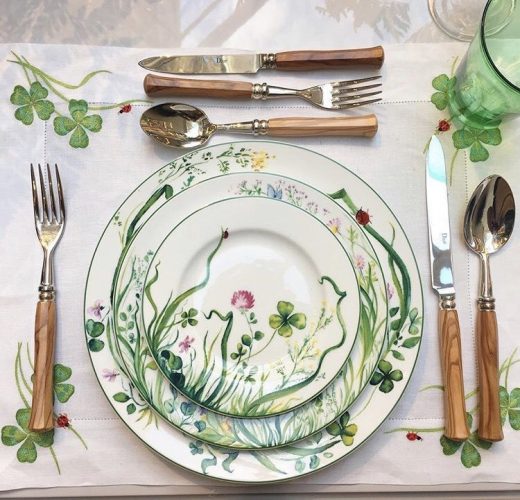 mesa posta com toalha branca com bordados, pratos brancos com estampa de flores e talheres com cabo de madeira. da grife francesa Dior