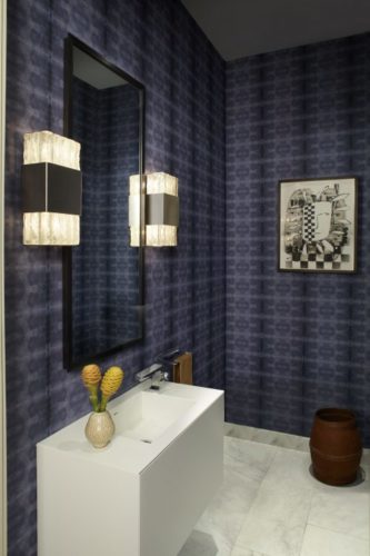 Loft em NY, lavabo com com paredes revestidas de tecido azul, luminárias art decor e bancada branca.