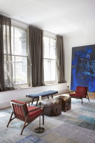 Loft em NY, poltronas vintage Joaquim Tenreiro, janelas amplas com cortina cinza e tela azul ao fundo da sala