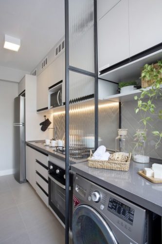Pequeno apartamento de 27m² em Piedade, Zona Norte do Rio de Janeiro, prova que é possível viver com conforto e praticidade em espaços reduzidos. Divisória em esquadria preta separa área de serviço e cozinha.