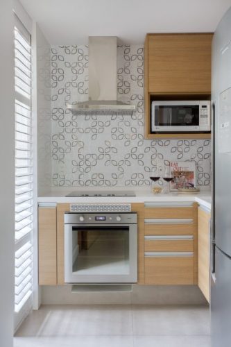 Pequenas interferências para tornar os ambientes mais amplos em um apartamento no Leblon. Pequena cozinha com cooktop, coifa e armários em madeira