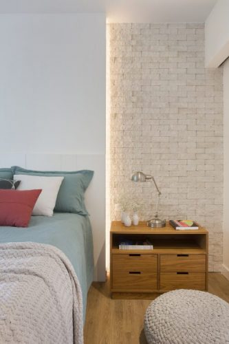 Pequenas interferências para tornar os ambientes mais amplos em um apartamento no Leblon. Painel branco atras da cama com luz embutida e lateral com tijolinho pintado de branco