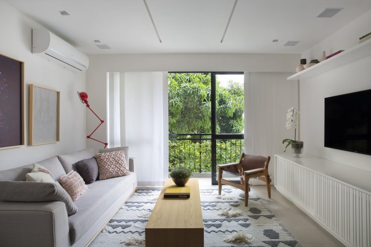 Pequenas interferências para tornar os ambientes mais amplos em um apartamento no Leblon. Paredes brancas, rack tv com ripado branco e varanda com cortina em voal.
