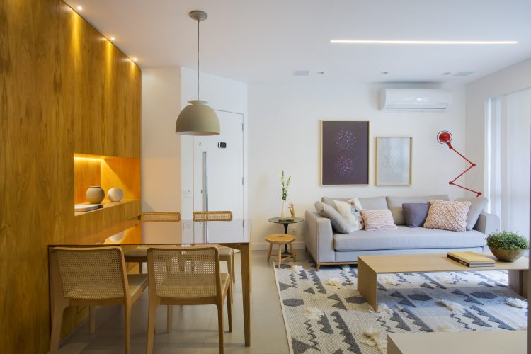 Pequenas interferências para tornar os ambientes mais amplos em um apartamento no Leblon. Sala com paredes brancas e parede lateral revestida em madeira