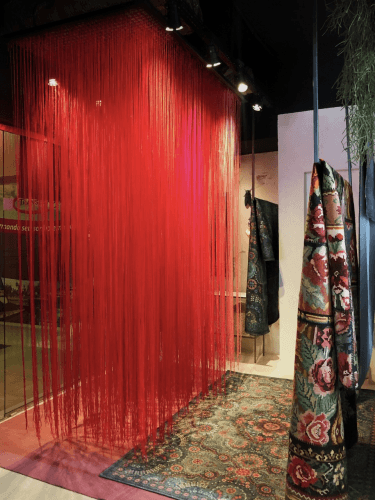 Vitrine de uma loja de tapetes, instalação com fios de lã na cor vermelha, vários fios pendurados um a um.
