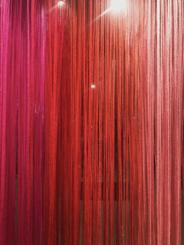 Vitrine de uma loja de tapetes, instalação com fios de lã na cor vermelha, vários fios pendurados um a um.