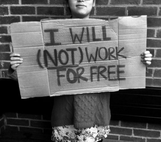 Jovem segura um cartaz feito de papelão escrito em inglês:  I will not work for free, tradução livre; eu não trabalho de graça.