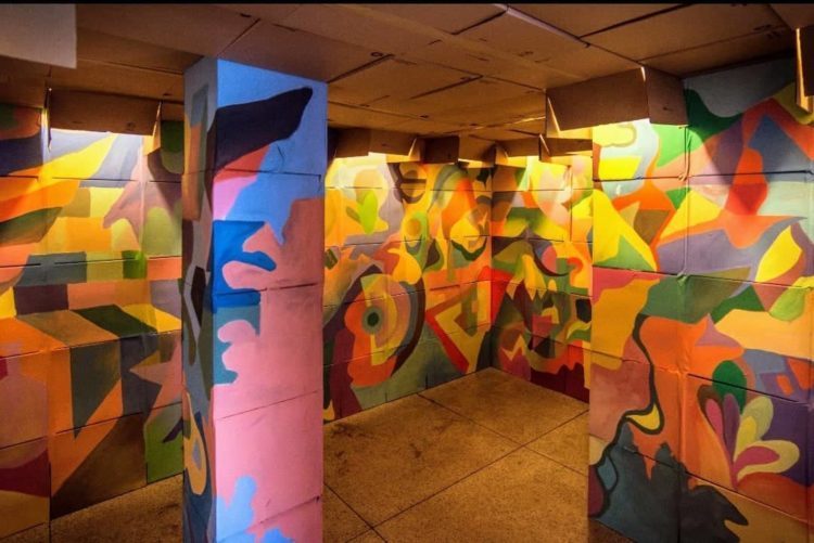Instalação artistica, 700 caixas pintadas , coloridas com desenhos geométricos  de papelão empilhadas criando um túnel 