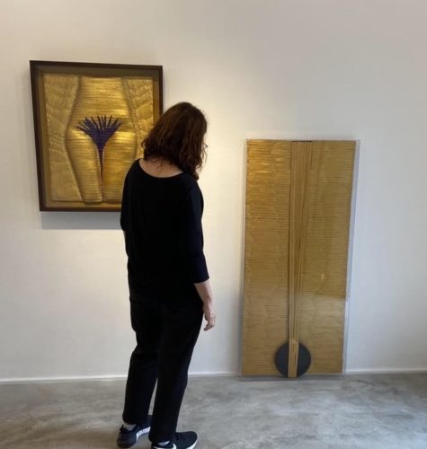 Foto da artista plastica Anna Paola Protasio vestida de preto e de costas arrumando a sua exposição